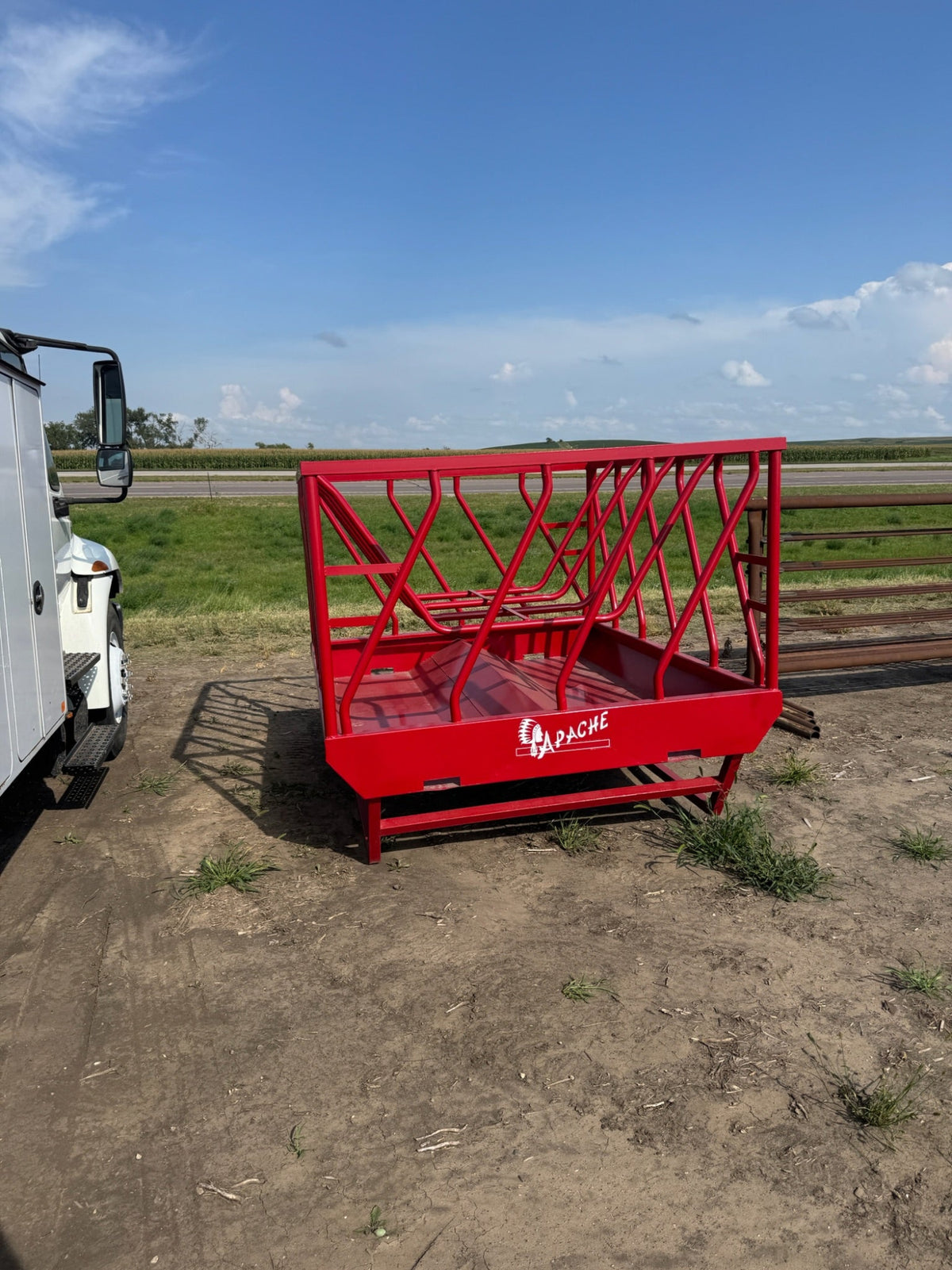 Red agricultural feed rack on a dirt field with a blue sky.