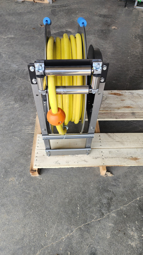 A yellow hose reel wound around a black metal reel, resting on a wooden pallet over a concrete floor.