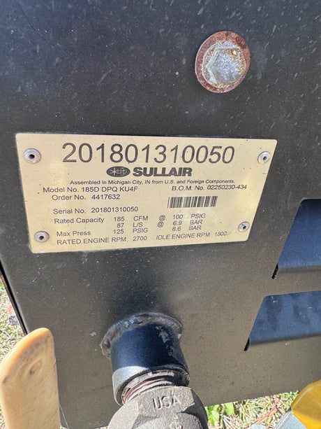 A close-up of a SULLAIR engine B.O.M. plate with serial number and attached to a dark metal engine block.
