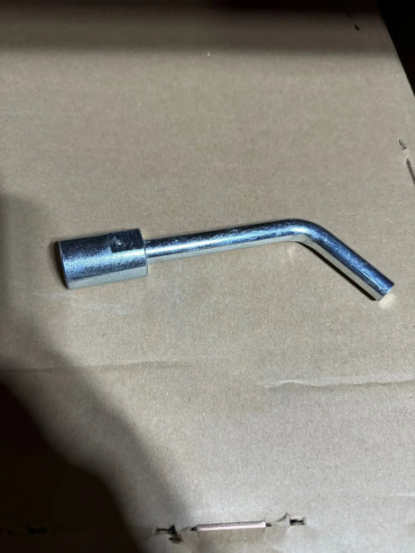 A silver metal hex wrench socket tool lying on a brown cardboard surface.